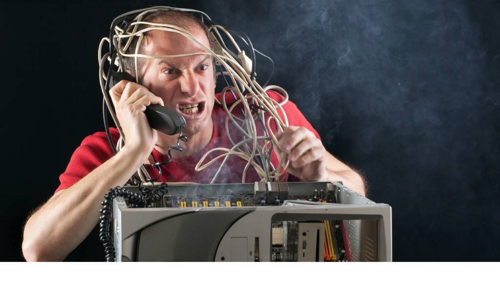 man frustrated on the phone with a broken computer in front of him