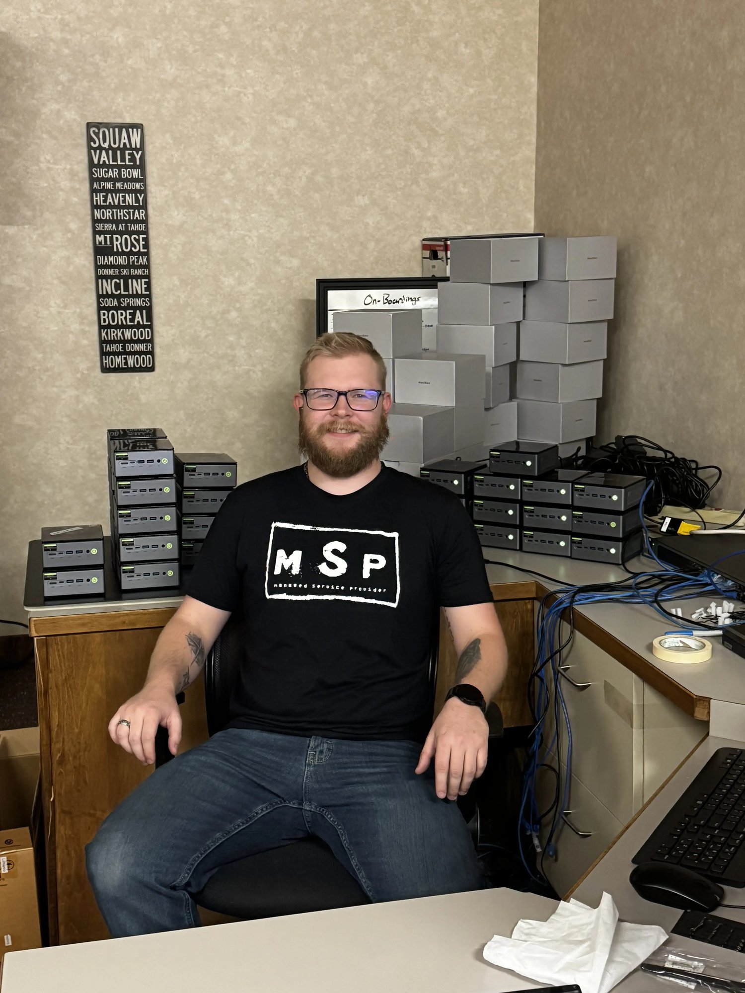 An IT engineer sitting at a desk with a black shirt that says MSP